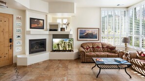 A living room with a fireplace, television, sofa, and large windows. - Red Rock Views, Hot Tub, Community Pool, Walk To Pickleball Court, Trail Pass (Sedona)