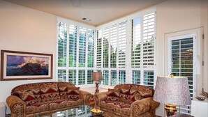 A living room with two patterned sofas, a glass coffee table, a lamp, and large windows with shutters. - Red Rock Views, Hot Tub, Community Pool, Walk To Pickleball Court, Trail Pass (Sedona)