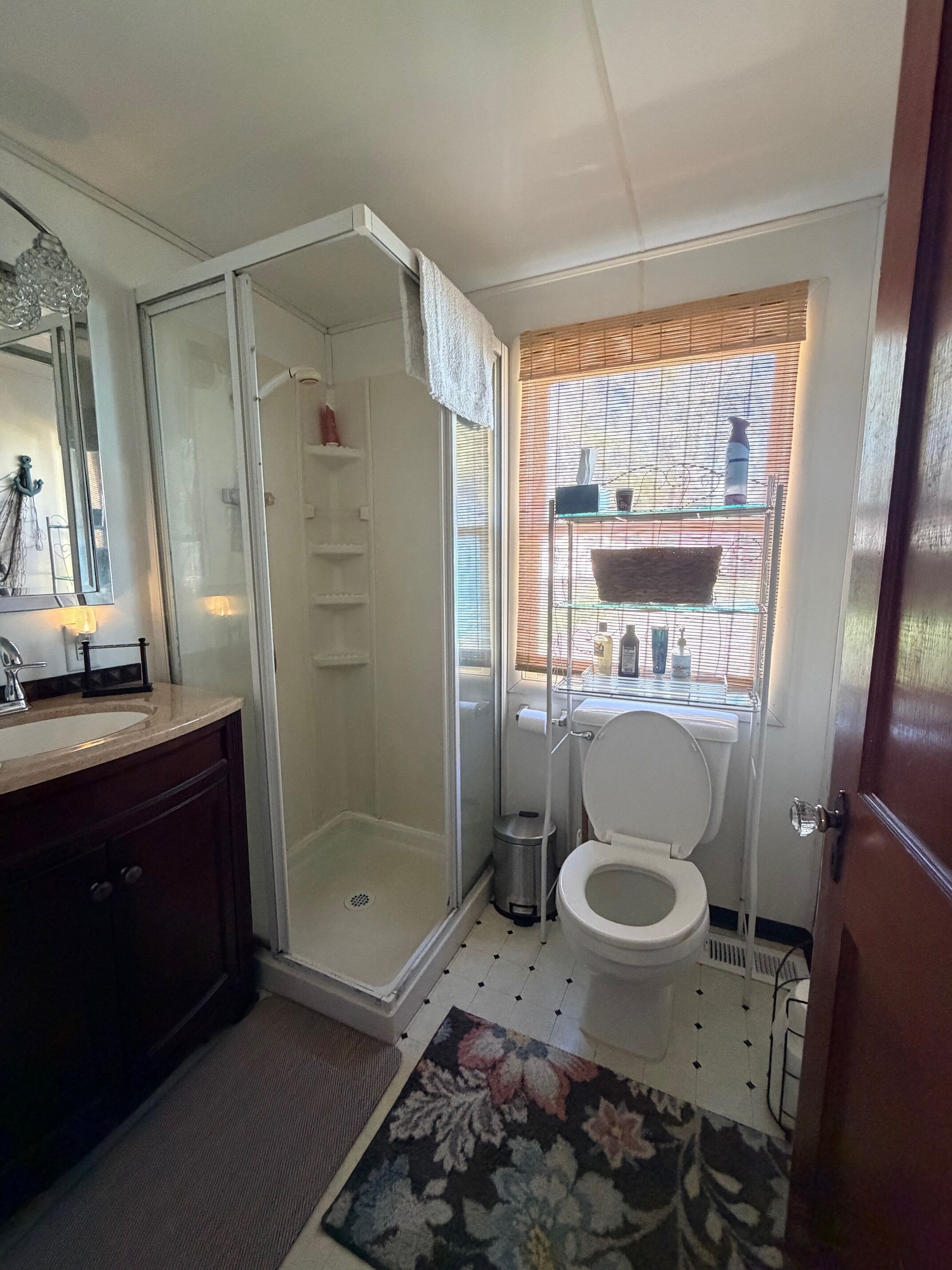A bathroom with a shower, toilet, sink, and a window with blinds.
