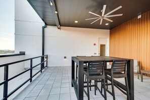 An outdoor terrace with a table and chairs, a railing, and a ceiling fan. - Downtown Skyline Views | Rooftop Deck | Walk to (Nashville)