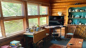 L’intérieur chaleureux d’un chalet, avec un décor en bois, un canapé, un bureau, un téléviseur et une étagère ornée d’objets décoratifs.