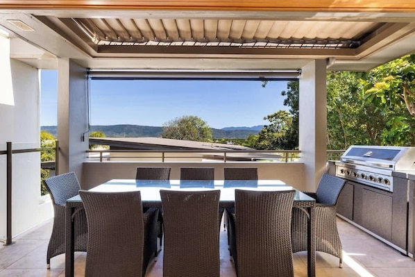 An outdoor patio with a table and chairs, a grill, and a view of the landscape.