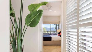A hotel room with a bed, a view of the outdoors, a ceiling fan, and a plant.