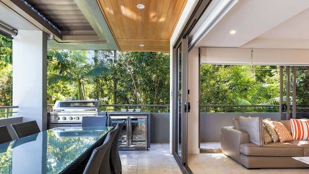 An outdoor dining area with a glass table and chairs, a grill, and a sofa with cushions.