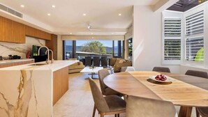 A modern kitchen with a marble countertop, a dining area with a wooden table and chairs, and large windows offering a view of the outdoors.