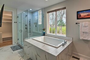A modern bathroom with a glass-enclosed shower, a large bathtub, and a window providing a view of trees. - Beautiful Nashville Home Near Downtown w/ Hot Tub! (Nashville)