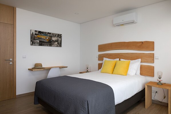 A bedroom with a bed, wooden headboard, bedside tables, a wall-mounted air conditioner, and a picture frame.