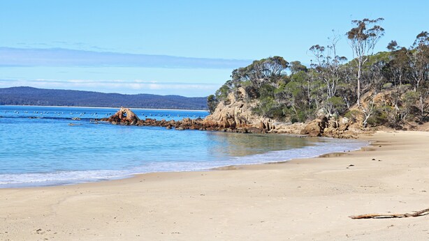 Ein Strand mit klarem, blauem Wasser, Sandstrand und Felsen.