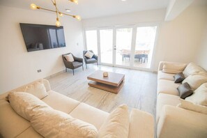 A modern living room with a sofa, armchairs, a coffee table, and a TV mounted on the wall.