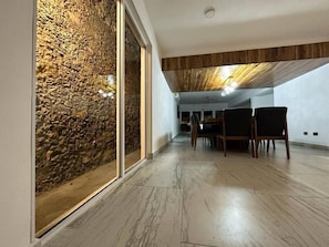 A modern interior with a stone wall, wooden ceiling, and a dining area with chairs and a table.