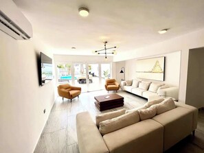 Een moderne woonkamer met een bank, fauteuils, een salontafel en een televisie.