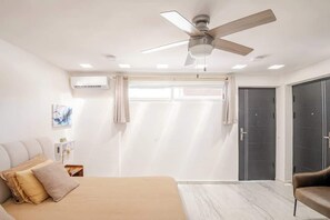 Une chambre à coucher comprenant un lit, un ventilateur de plafond, un appareil de climatisation, une fenêtre avec des rideaux et une porte.