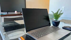 Una computadora portátil sobre una mesa de vidrio, con una planta y un ratón cerca.
