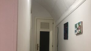 Un couloir étroit au sol carrelé, une porte blanche dotée d’une grille d’aération et un banc en bois sur la droite.