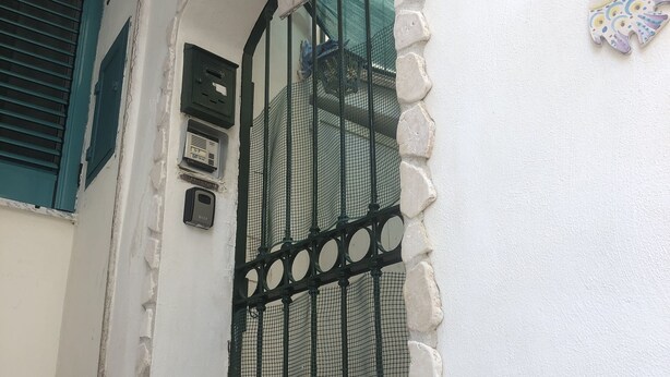 Un bâtiment blanc avec un portail en métal noir, une porte bleue et le numéro « 21 » peint sur le mur.