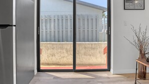Une pièce dotée d’une porte-fenêtre coulissante donnant sur un balcon, d’un réfrigérateur et d’un journal encadré accroché au mur.