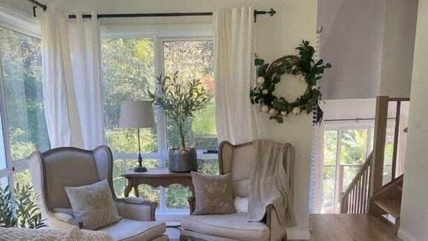 A cozy living room with a sofa, two armchairs, a coffee table with decorative items, and a view of greenery outside. - Sunny Corner - Romantic Split Level Cottage (Leura)