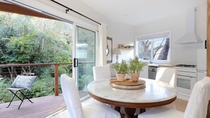 A modern kitchen with a large window, a dining area with a round table and chairs, and a balcony with a chair. - Sunny Corner - Romantic Split Level Cottage (Leura)