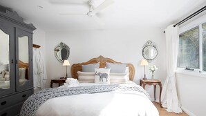 A bedroom with a large bed, a wardrobe, two bedside tables, a ceiling fan, and a window with curtains. - Sunny Corner - Romantic Split Level Cottage (Leura)
