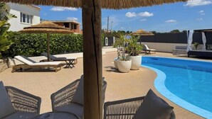 Ein Poolbereich mit Liegestühlen, einem Reetdachschirm und Kübelpflanzen.