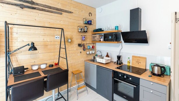 A compact kitchen with a wooden wall, a black stove, and a small sink. - HAPPY HOME HELSINKI-KALLIO (Helsinki)