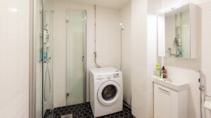 A compact bathroom with a glass shower enclosure, a built-in washing machine, and a small vanity with a mirror. - HAPPY HOME HELSINKI-KALLIO (Helsinki)