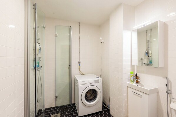 A compact bathroom with a glass shower enclosure, a built-in washing machine, and a small vanity with a mirror.