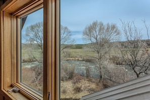 Enjoy breathtaking views of the surrounding landscape from this room's window, overlooking a serene river, trees, and rolling hills.