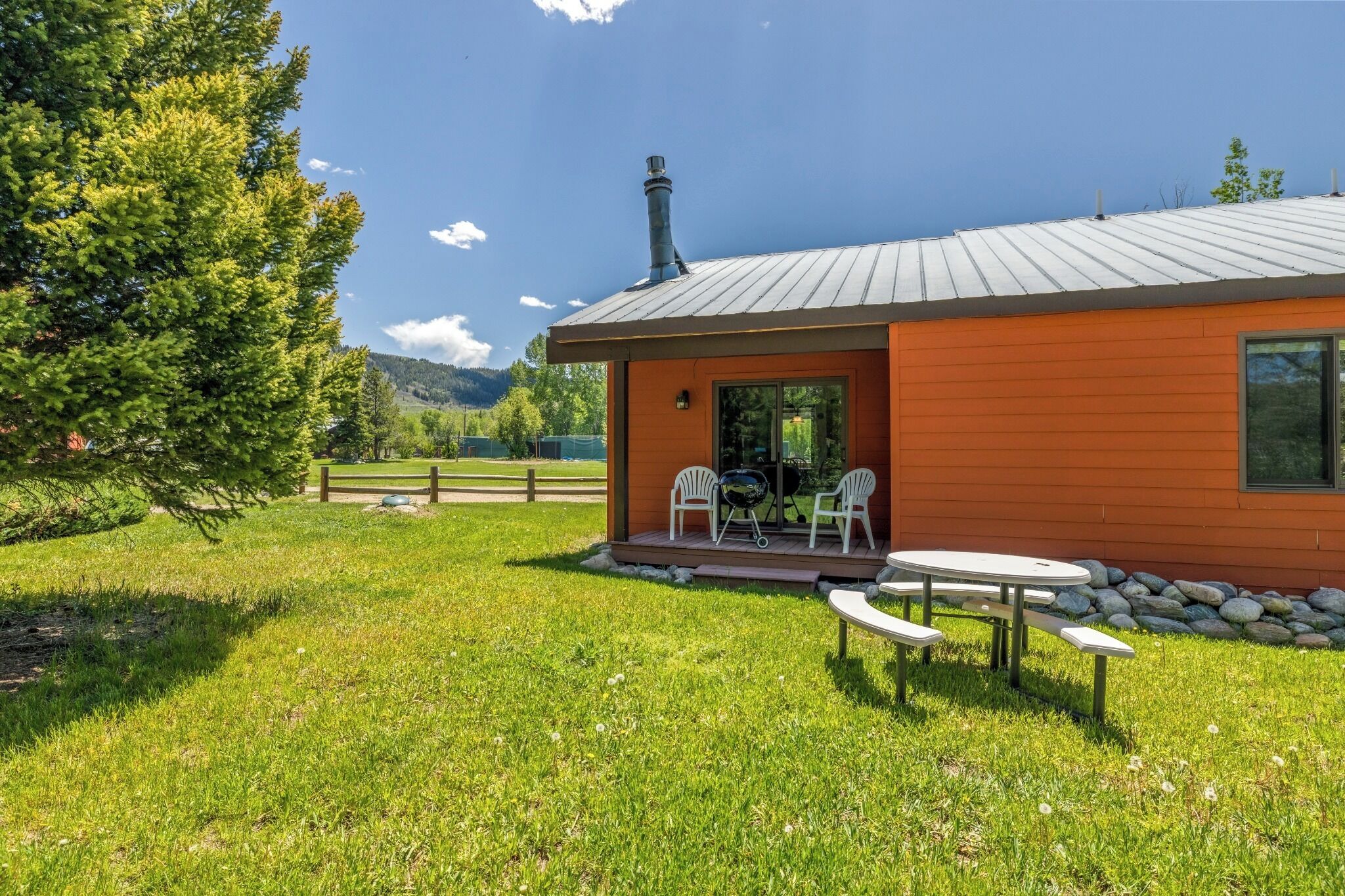Une cabane en bois avec un toit en métal, une cheminée et une terrasse dotée de meubles d’extérieur.