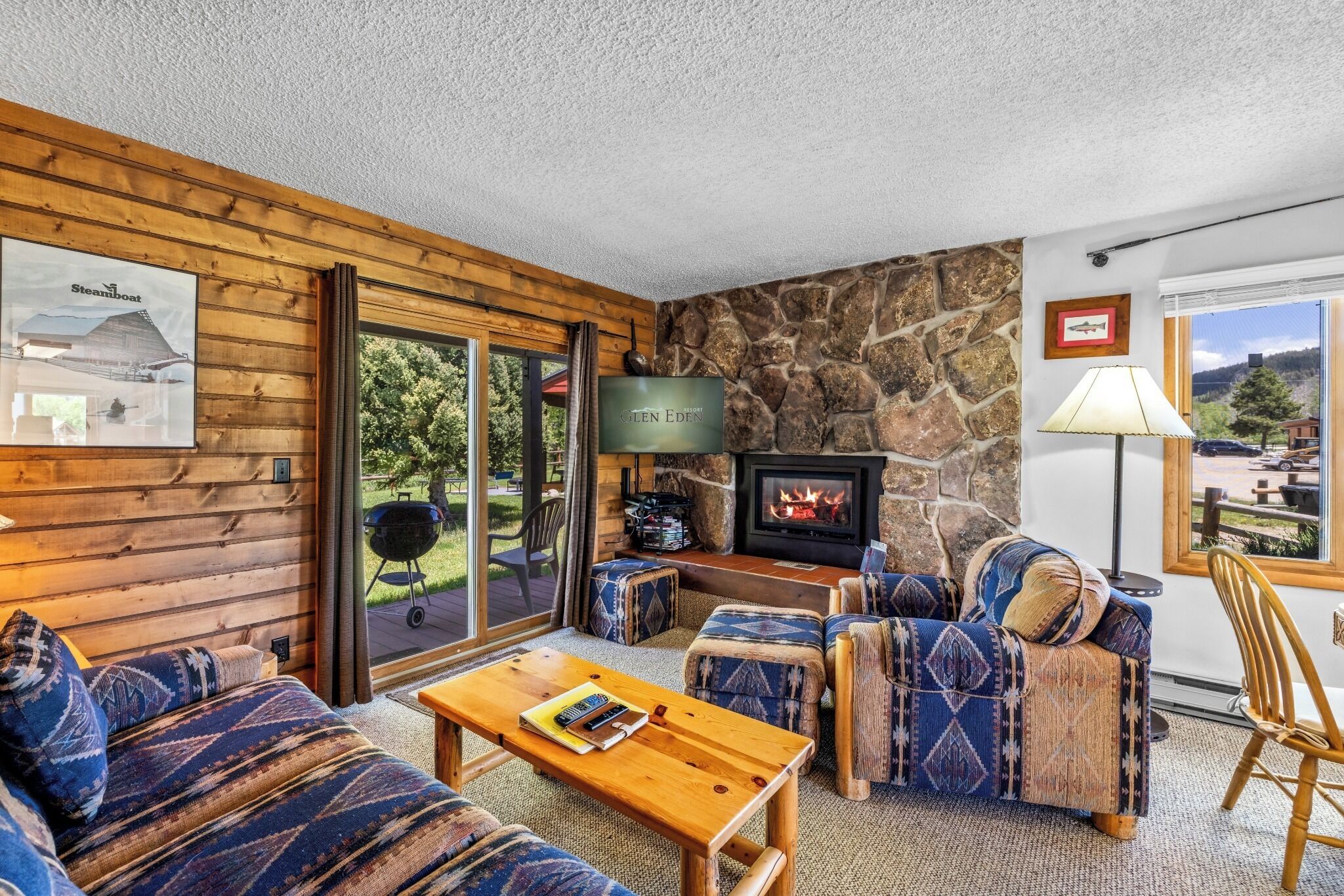 A cozy room with a stone wall, a fireplace, a television, and a view of the outdoors.