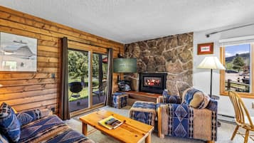 A cozy room with a stone wall, a fireplace, a television, and a view of the outdoors.