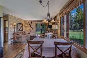 A cozy living room with a large window, wooden furniture, and a chandelier. - Pioneer - Cozy riverside retreat in the mountains (Clark)