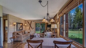 A cozy living room with a large window, wooden furniture, and a chandelier. - Pioneer - Cozy riverside retreat in the mountains (Clark)