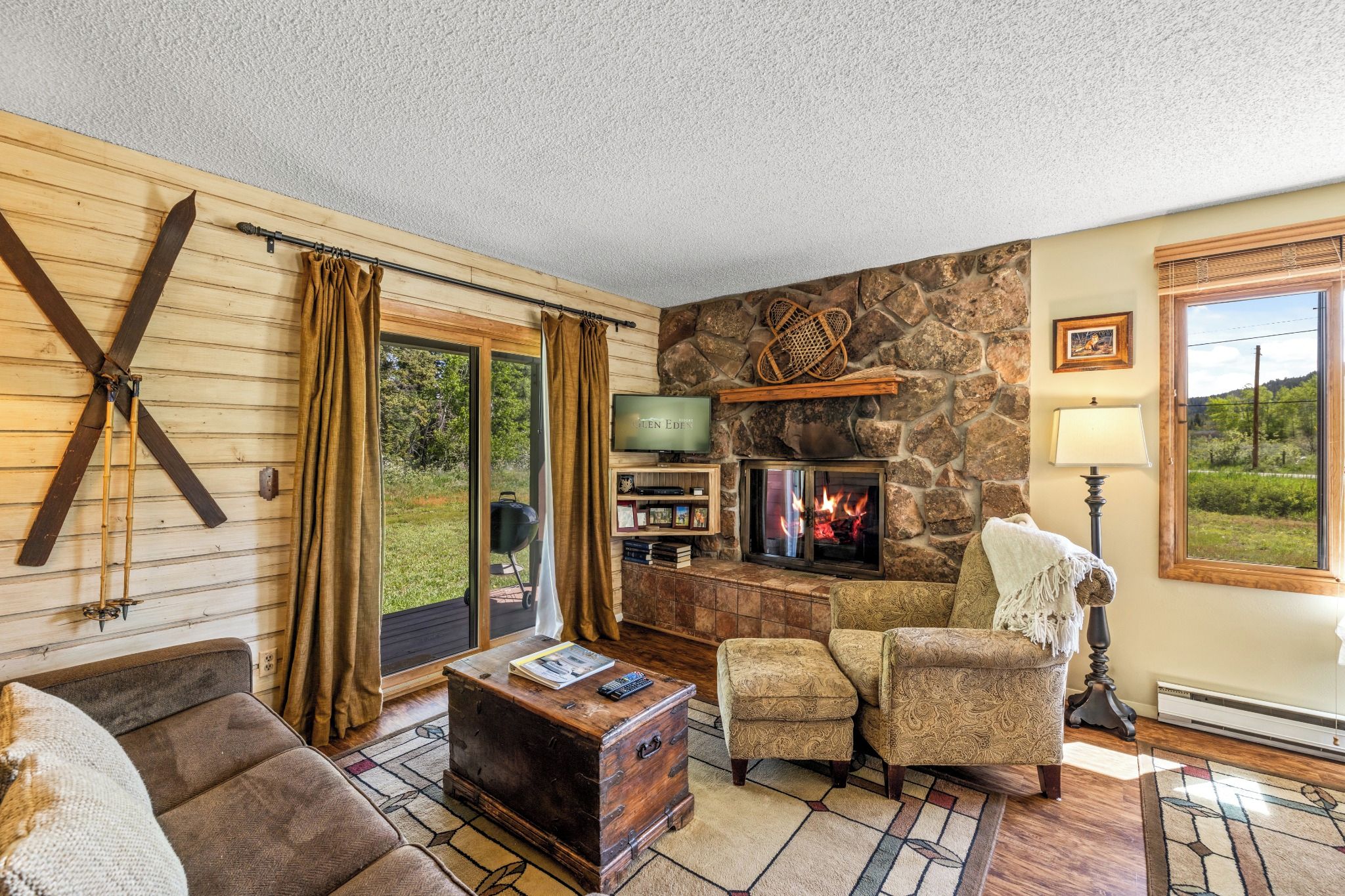 A cozy living room with a stone fireplace, wooden furniture, and a view of the outdoors.