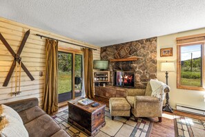 A cozy living room with a stone fireplace, wooden furniture, and a view of the outdoors. - Pioneer - Cozy riverside retreat in the mountains (Clark)