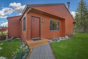 A wooden cabin with a red door, a nameplate, and a small porch. - Pioneer - Cozy riverside retreat in the mountains (Clark)