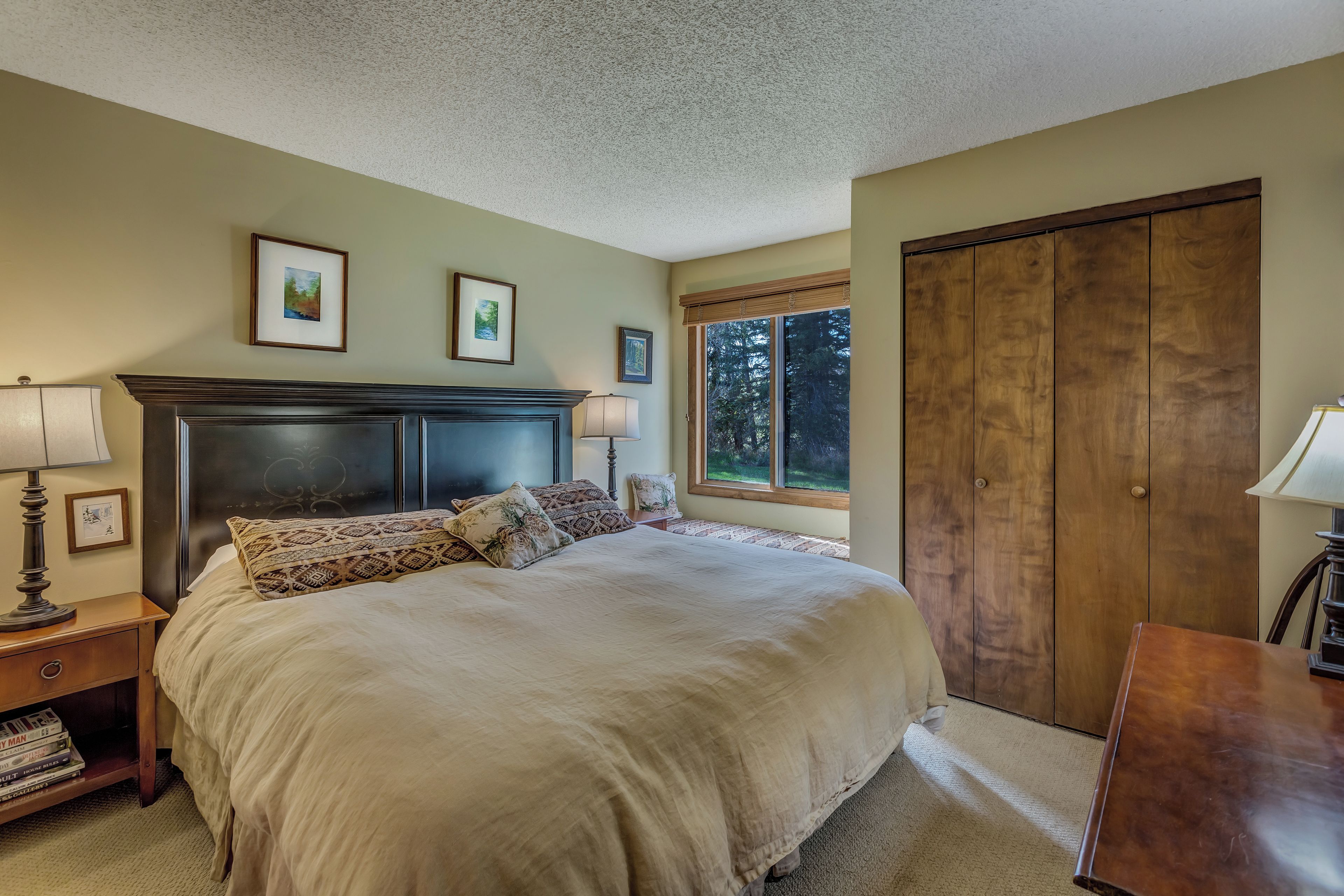 Une chambre à coucher avec un grand lit, une armoire en bois, une table de chevet avec une lampe et des tableaux encadrés accrochés au mur.
