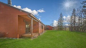 A wooden cabin with a porch, a clear sky, and a grassy yard. - Pioneer - Cozy riverside retreat in the mountains (Clark)