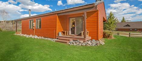 A single-story wooden cabin with a chimney, large windows, and a stone foundation.