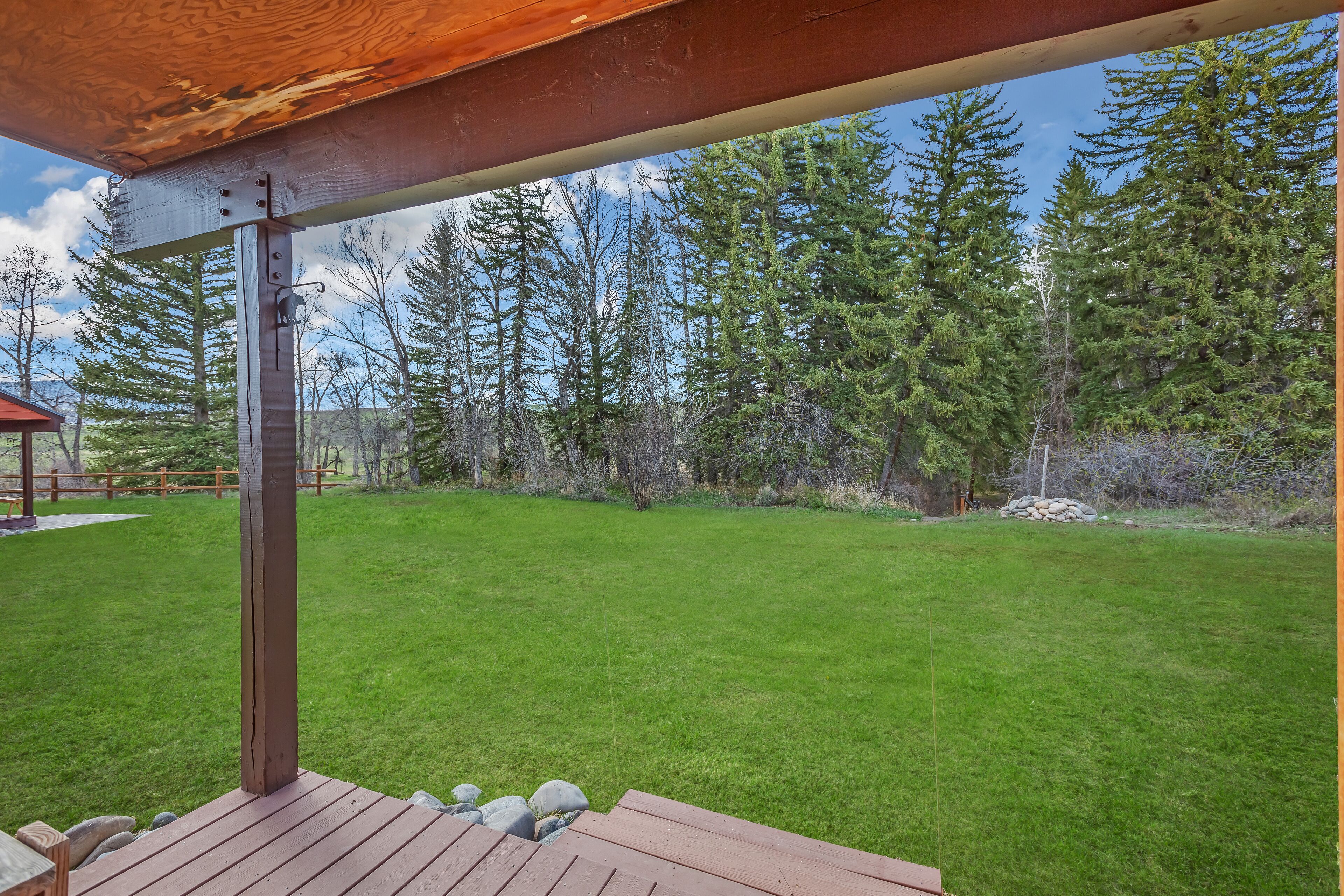 A wooden deck with a view of a grassy yard and tall trees.
