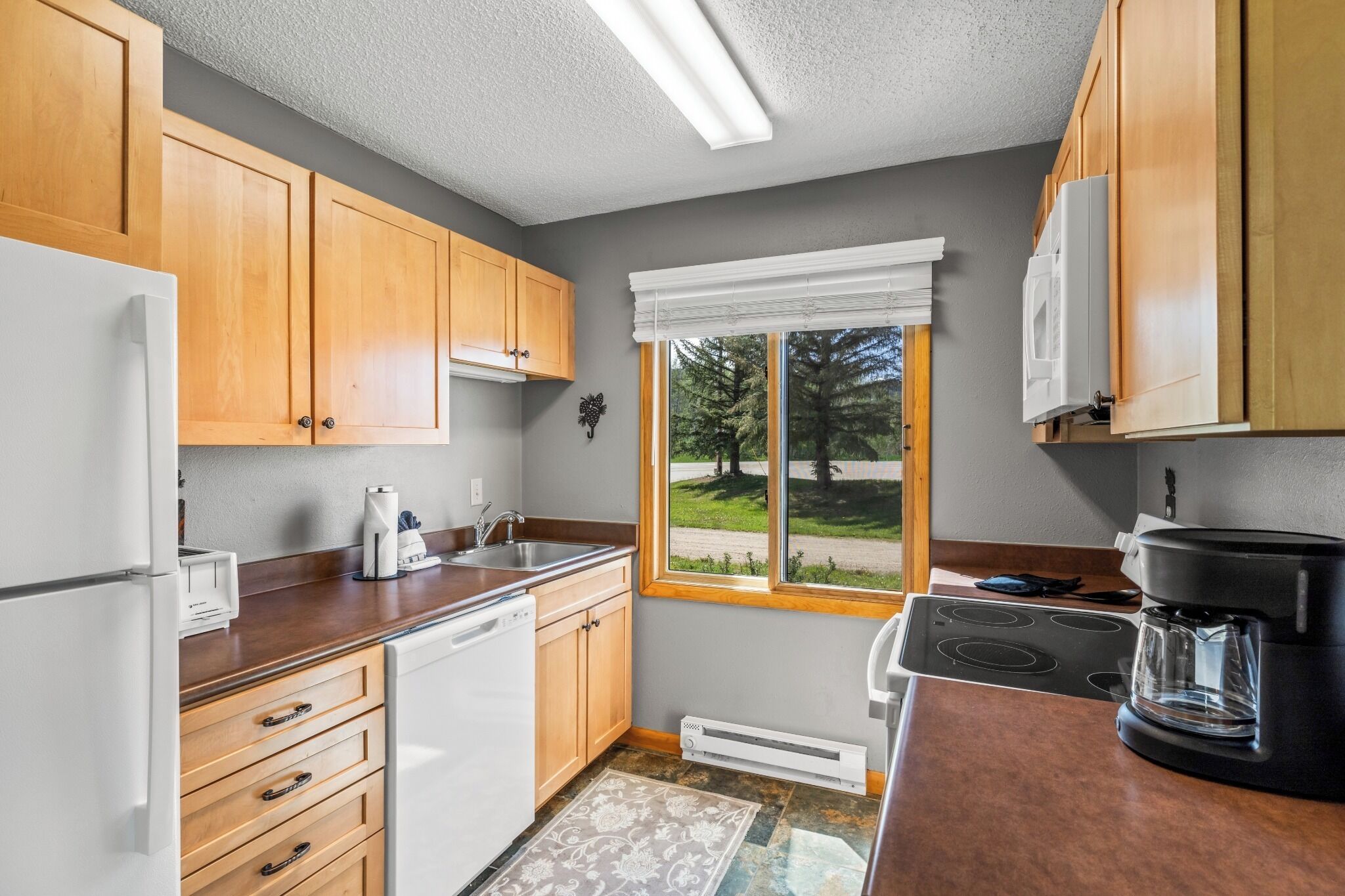 A kitchen with wooden cabinets, a built-in dishwasher, a stove, and a window with a view of trees.