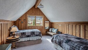 A cozy attic bedroom with two beds, a wooden bench, and a window offering a view of the countryside. - Honey Bear - Mountain cabin with gorgeous scenery (Clark)