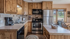 A kitchen with wooden cabinets, stainless steel appliances, a coffee maker, and a view of the outdoors. - Honey Bear - Mountain cabin with gorgeous scenery (Clark)