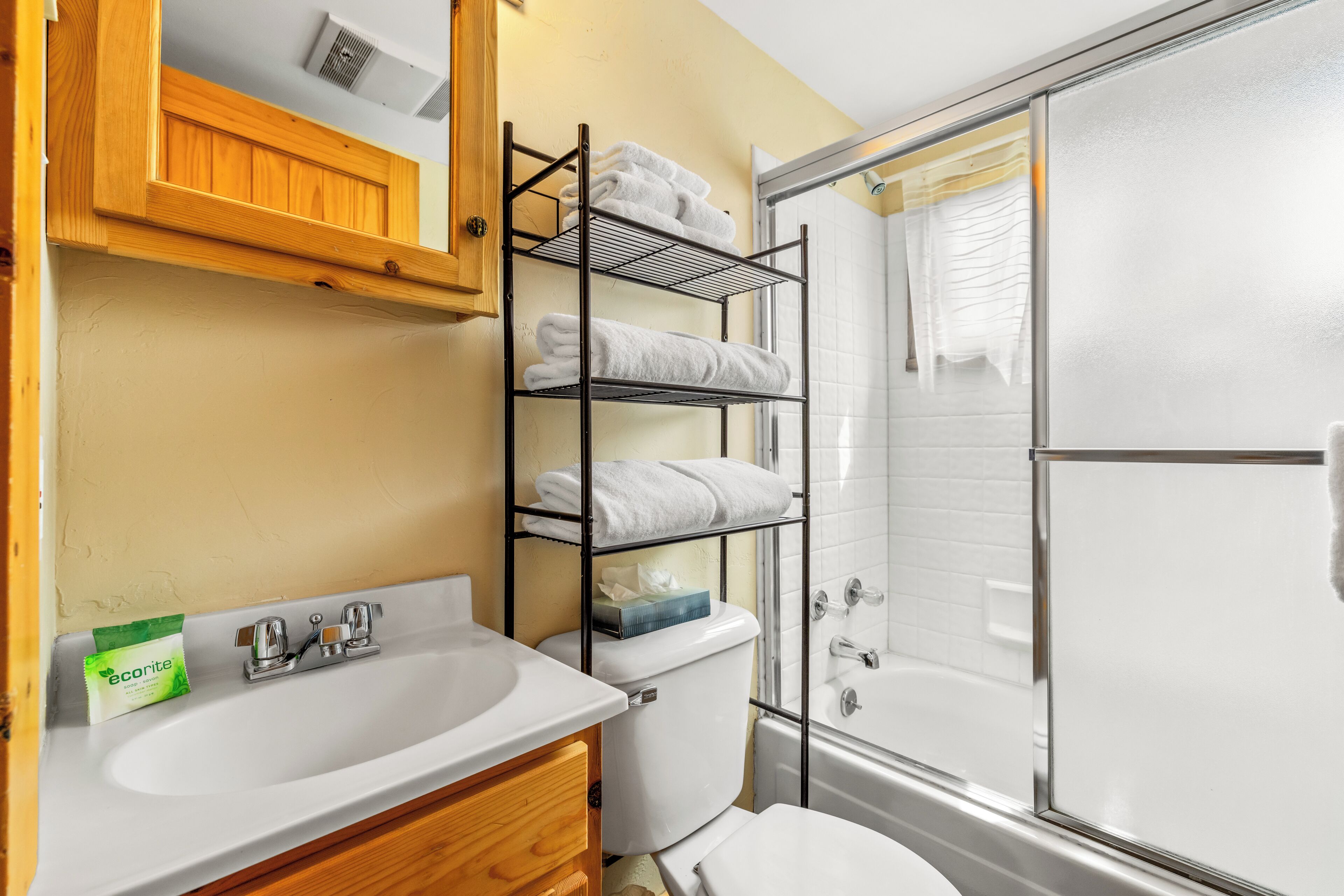 A bathroom with a white sink, a wooden cabinet, a towel rack, and a glass shower enclosure.