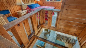 A wooden cabin with a loft bedroom, a dining area, and a view of the outside.