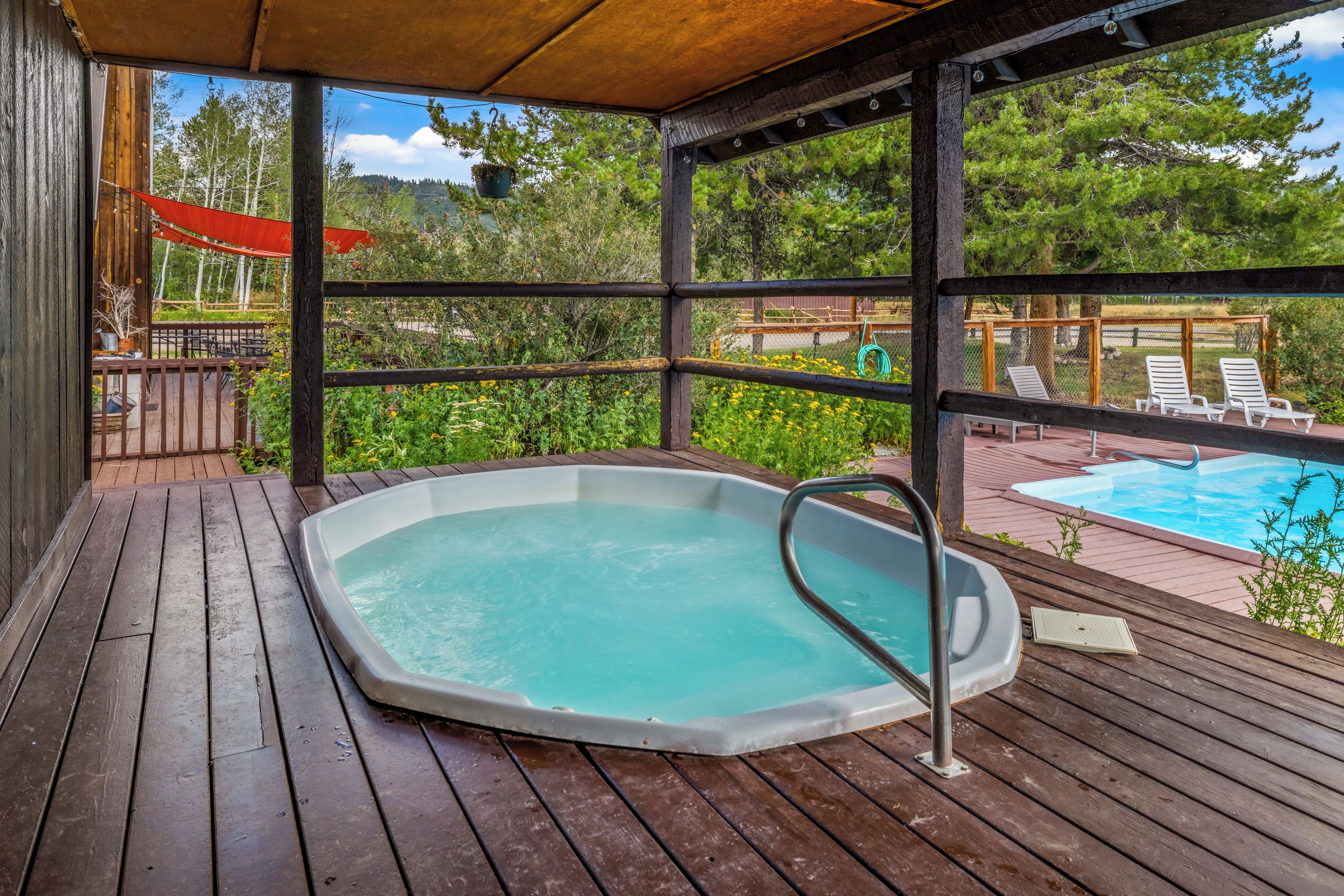 A wooden deck with a hot tub, outdoor seating, and a view of a swimming pool.