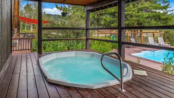 A wooden deck with a hot tub, outdoor seating, and a view of a swimming pool.