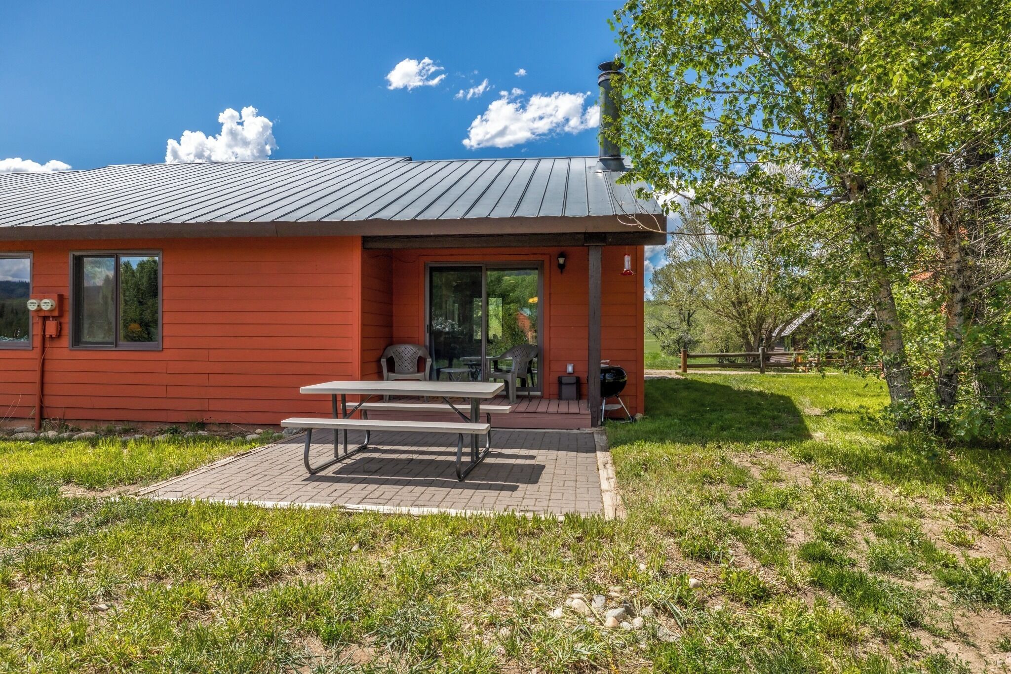 Un bâtiment rouge avec un toit en métal, une table de pique-nique et un barbecue à l’extérieur.