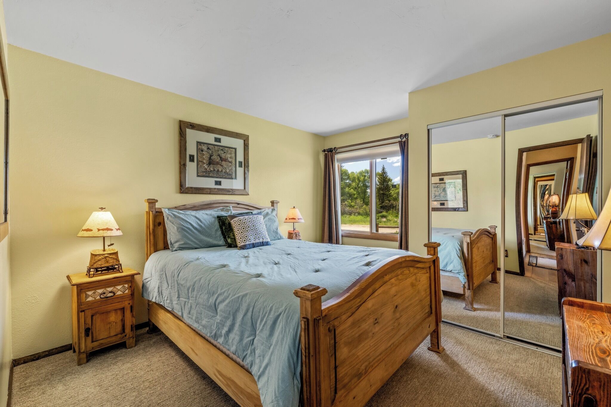Une chambre à coucher avec un grand lit, deux tables de chevet avec des lampes, un grand miroir et une fenêtre avec des rideaux.