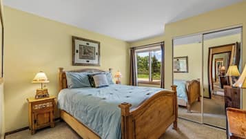 A bedroom with a large bed, two bedside tables with lamps, a large mirror, and a window with curtains.
